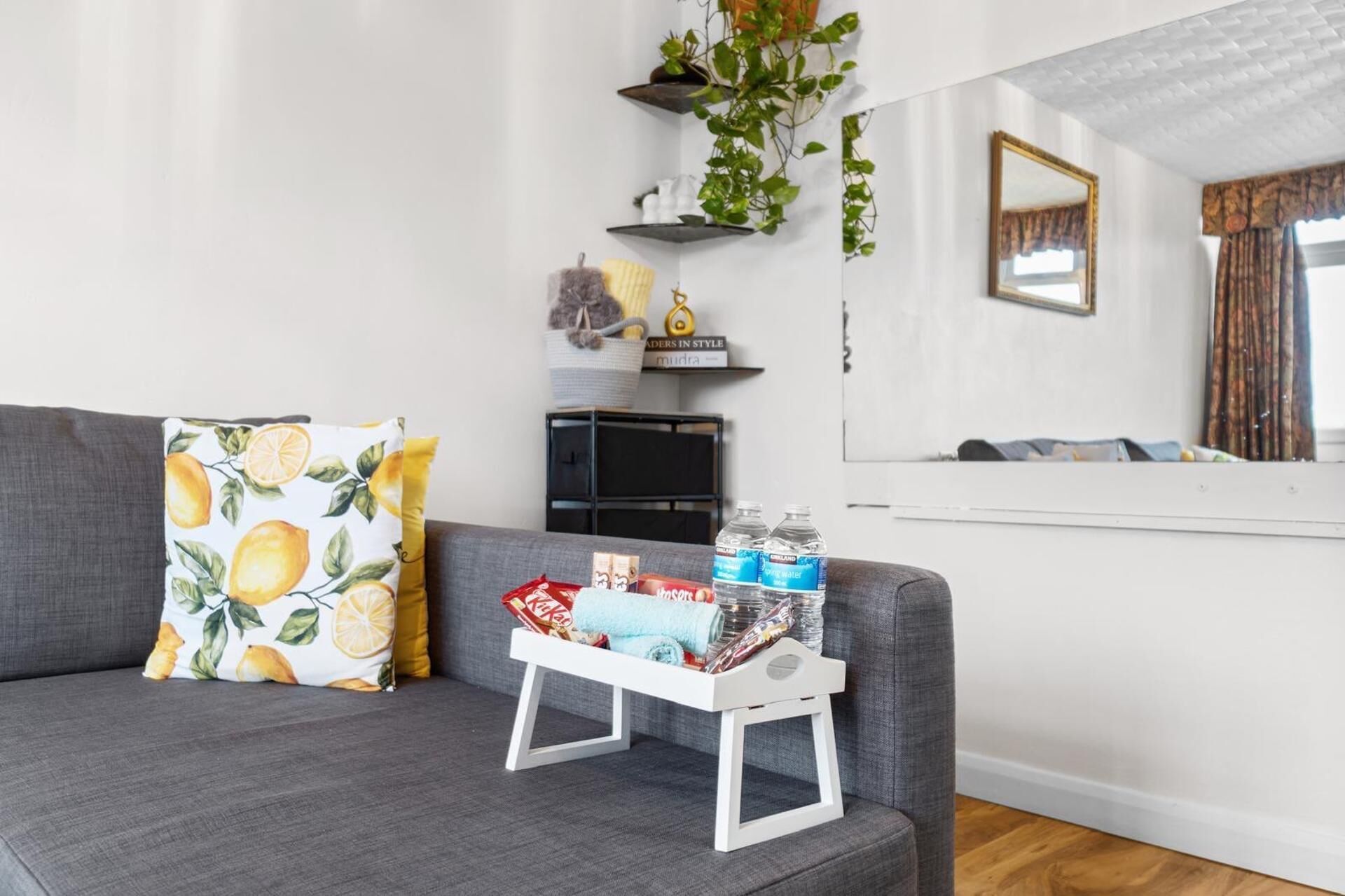 A living room with a grey sofa, a small white side table, and a mirror on the wall.