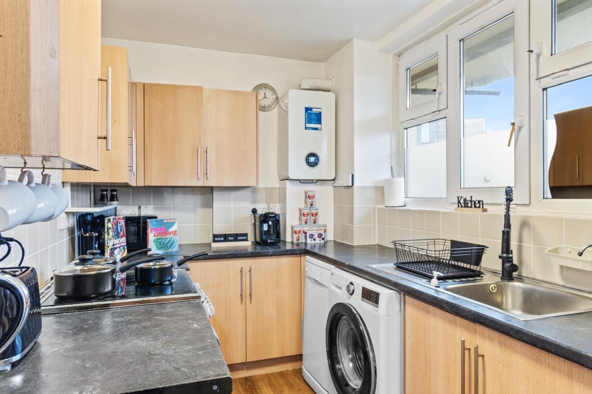 A compact kitchen with a washing machine, a coffee maker, and a kettle.