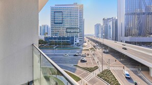 A high-rise building with a modern glass facade, a busy highway with multiple lanes, and a pedestrian crossing. - Brand New 1B With Burj Khalifa View in Business Bay (Dubai)