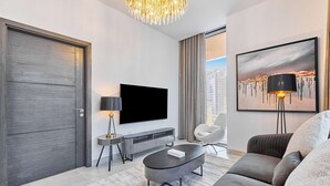 A modern living room with a flat-screen TV, a round coffee table, a sofa, and a painting on the wall. - Brand New 1B With Burj Khalifa View in Business Bay (Dubai)