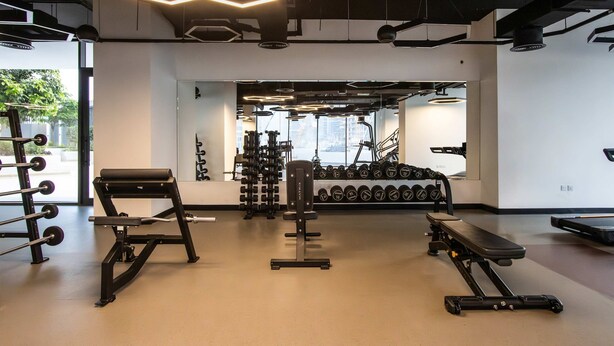 A modern gym with various exercise equipment, including a bench press, dumbbells, and a squat rack. - Brand New 1B With Burj Khalifa View in Business Bay (Dubai)