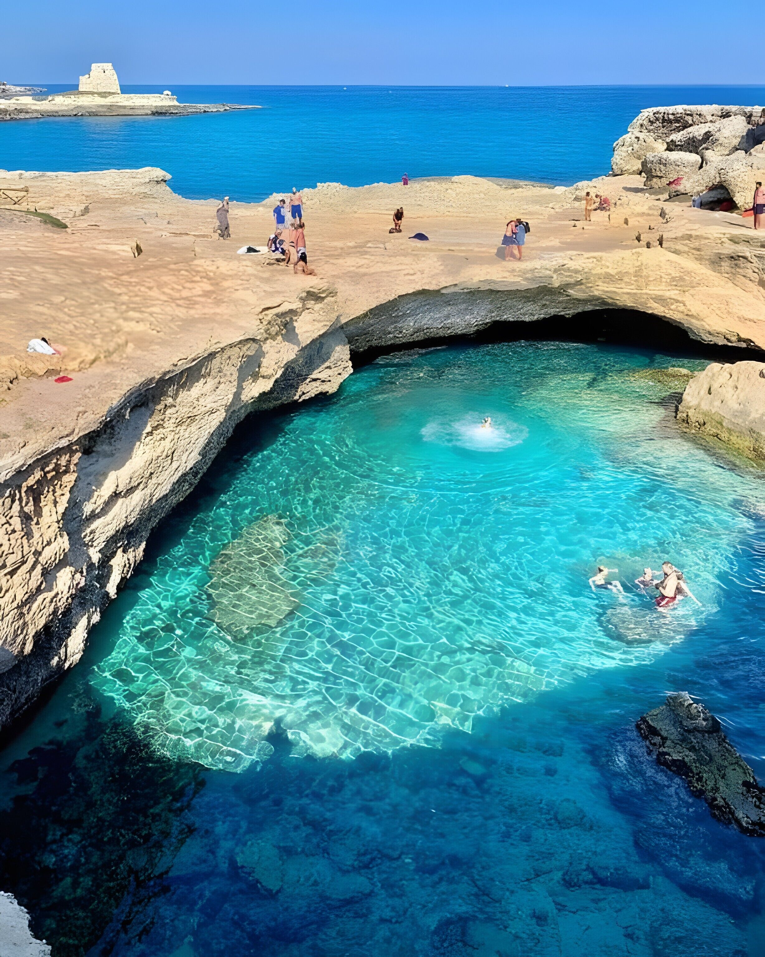 A natural pool with clear water, surrounded by rocky terrain and a view of the sea.