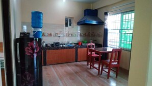 Una cocina con refrigerador, dispensador de agua, estufa y ventana con rejas.