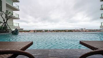 Vista de la piscina con sillas de descanso, una estatua y el paisaje urbano al fondo.