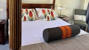 A four-poster bed with floral pillows, a striped rug, and a decorative pillow on the bed.