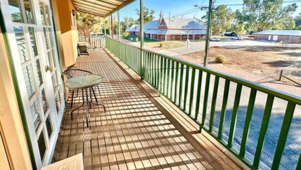A covered veranda with a wooden floor, a glass table, and a green railing.