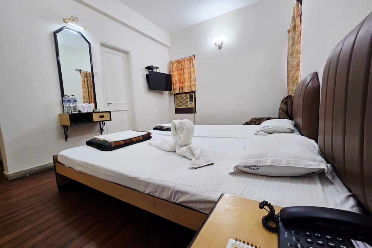 Habitación de hotel con una cama, un escritorio con teléfono, un espejo, televisión y una ventana con cortinas.