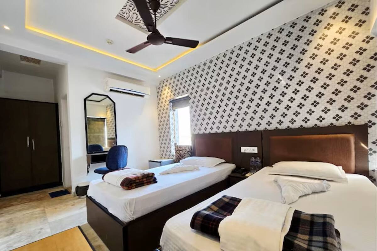 Habitación de hotel con dos camas, ventilador de techo, armario, espejo y papel tapiz estampado.
