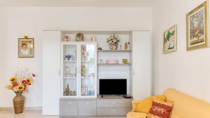 Una sala de estar con un sofá, un aparador con puertas de vidrio, un televisor y un florero con flores.
