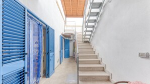 Un estrecho pasillo con contraventanas azules, una escalera y vistas al cielo.