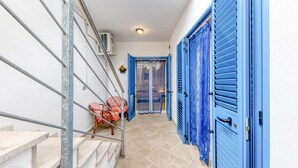 Un pasillo estrecho con contraventanas azules, una escalera y una silla.
