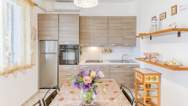 Una cocina moderna con armarios de madera, un refrigerador de acero inoxidable, una mesa de comedor con un florero y una lámpara colgante.
