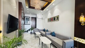 A modern living room with a sofa, a coffee table, and a TV mounted on the wall. - MG Plaza Hotel (Jodhpur)