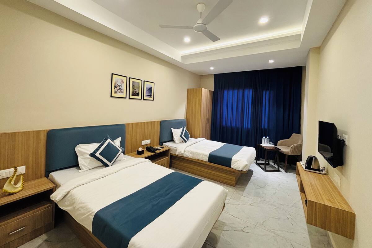 A hotel room with two beds, a desk, a chair, a ceiling fan, and a TV.