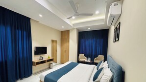 A modern hotel room with a large bed, a flat-screen TV, a desk with a kettle, and a ceiling fan. - MG Plaza Hotel (Jodhpur)