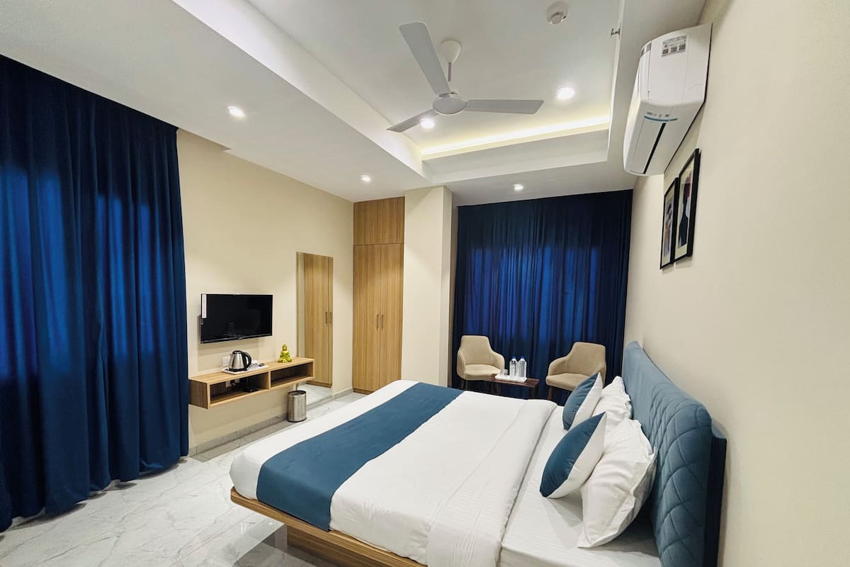 A modern hotel room with a large bed, a flat-screen TV, a desk with a kettle, and a ceiling fan.