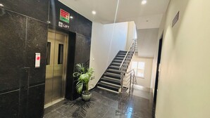 A modern elevator with a lift button, a staircase, and a potted plant in a lobby area. - MG Plaza Hotel (Jodhpur)