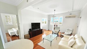 A spacious living room with a flat-screen TV, a glass coffee table, a beige sofa, and a white armchair. - RAG25 - Balmoral Beach Lifesaver – Executive Listing (Mosman)