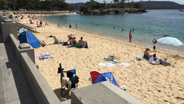A beach with people sunbathing and swimming, a clear sky, and a rocky shoreline. - RAG25 - Balmoral Beach Lifesaver – Executive Listing (Mosman)