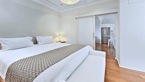 A hotel room with a large bed, a bedside table with a lamp, and a view into the kitchen area. - RAG25 - Balmoral Beach Lifesaver – Executive Listing (Mosman)