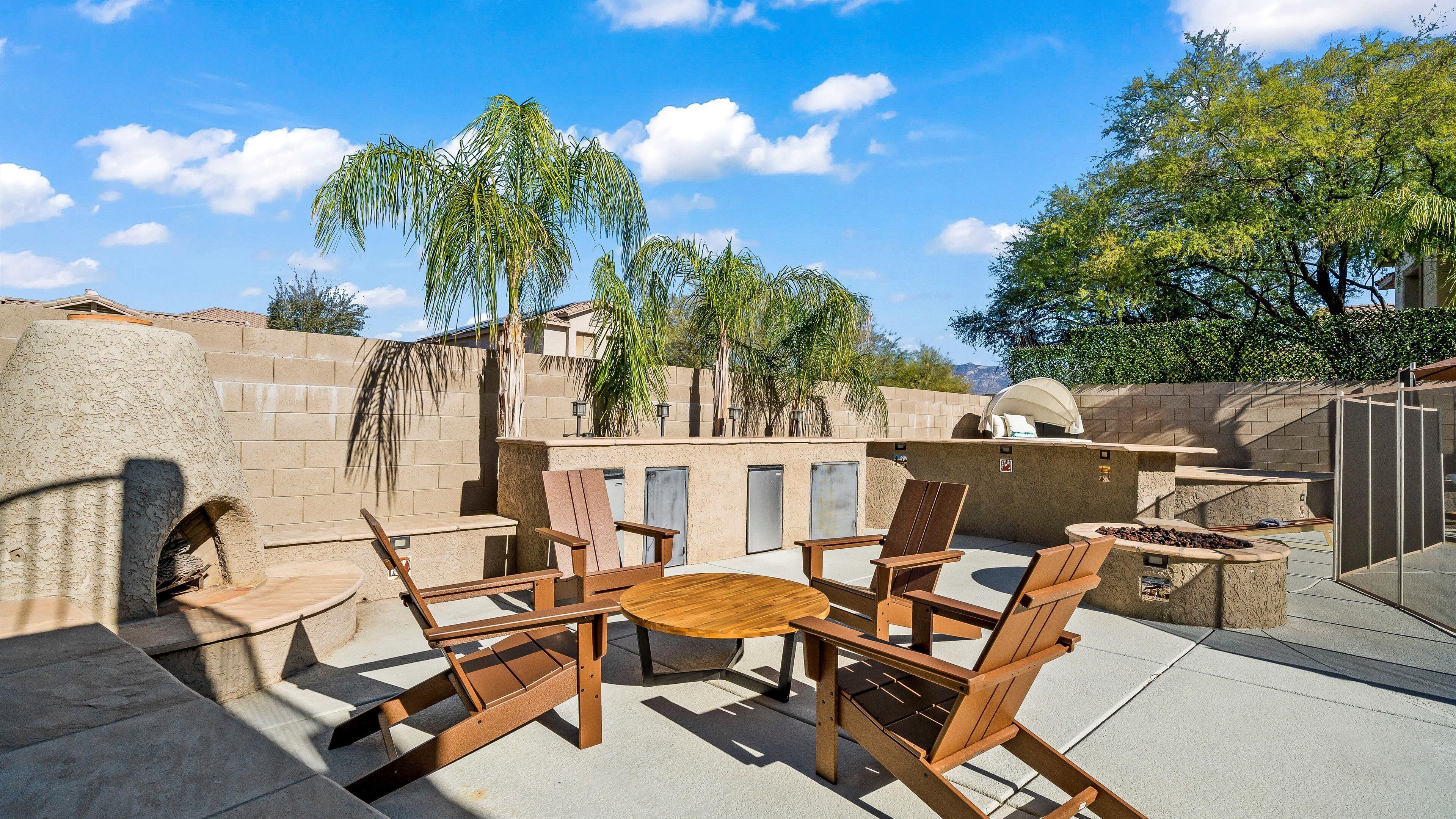 Een terras buiten met een ronde tafel en vier houten stoelen, een barbecue en een stenen muur.