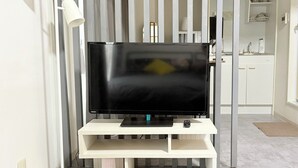 A flat-screen TV on a white stand in a room with a striped curtain background. - XeroB HOUSE FLOLIA601 (osaka naniwa ward nanbanaka)