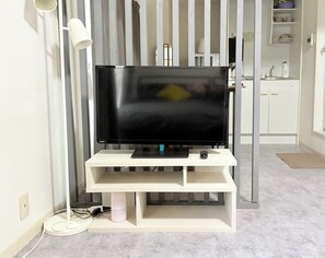 Ein Flachbildfernseher auf einem weißen Stand in einem Raum mit gestreifter Vorhangkulisse.