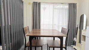 A dining area with a wooden table and chairs, a window with curtains, and a kitchen area with cabinets and appliances. - XeroB HOUSE FLOLIA601 (osaka naniwa ward nanbanaka)