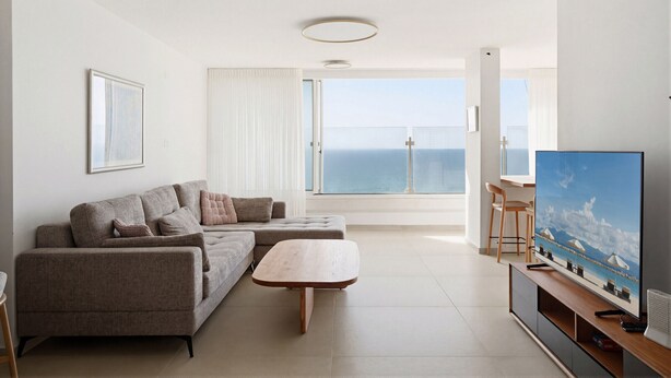 Una sala de estar moderna con un sofá, una mesa de centro, un televisor y vista al mar a través de un ventanal grande.