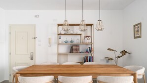 Un comedor con una mesa de madera y seis sillas, una estantería con objetos decorativos e iluminación colgante.