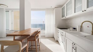 Una cocina moderna con armarios blancos, una mesa de comedor de madera y vistas al mar.