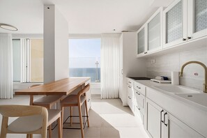 A modern kitchen with white cabinetry, a wooden dining table, and a view of the sea. - MIKLAT Family Friendly & Stunning Sea View by FeelHome (Netanya)