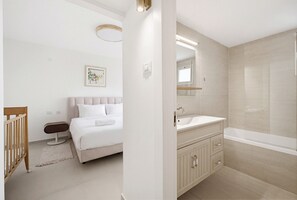 A modern bathroom with a bathtub, vanity, and a bed with a headboard. - MIKLAT Family Friendly & Stunning Sea View by FeelHome (Netanya)