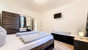 Quarto moderno com cabeceira de madeira, um espelho grande, uma TV de tela plana e uma mesa de cabeceira com abajur.