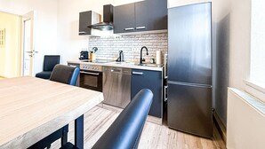 Uma cozinha compacta com mesa de jantar de madeira, um banco, forno embutido, máquina de lavar louça e frigorífico.