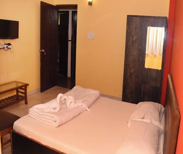 A hotel room with a bed, a bench, a TV, and a door leading to another room. - Alfina Guest House (Margao)
