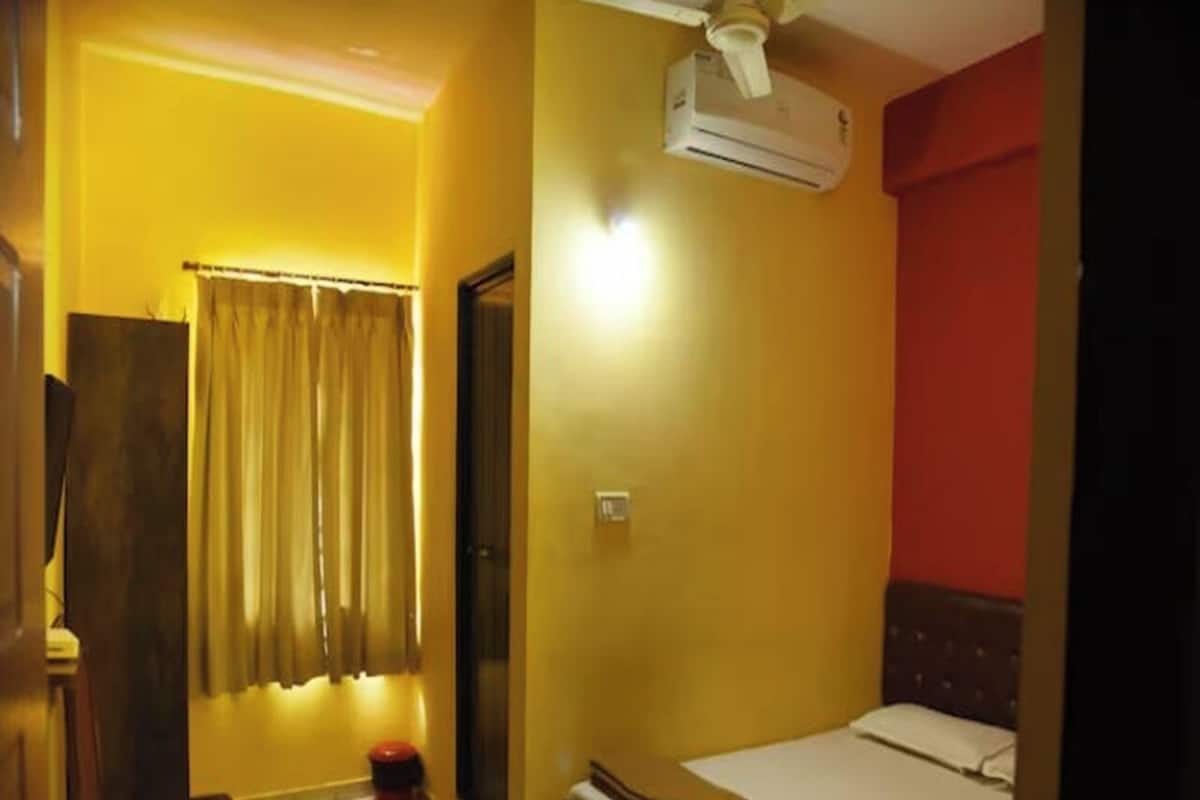 Una habitación pequeña con cama individual, ventilador de techo, aire acondicionado y una pared de acento roja.