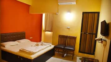 A bedroom with a bed, a chair, a television, and an air conditioning unit.