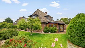 Una casa con techo inclinado, fachada de ladrillo y un jardín bien cuidado con diversas plantas y flores.