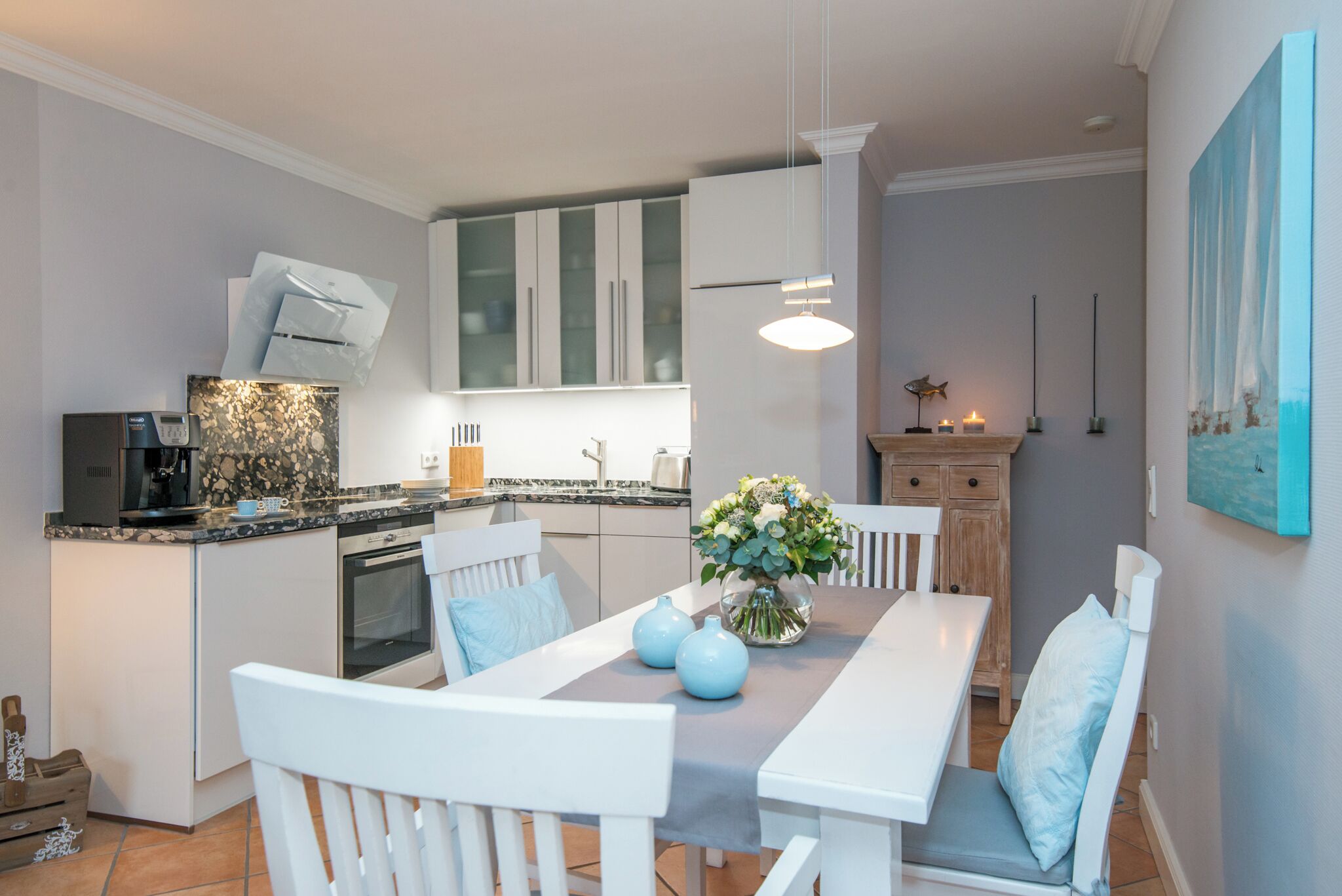 Una cocina moderna con armarios blancos, horno empotrado y comedor con mesa y sillas blancas.