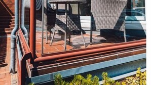 Varanda com cadeiras de vime, uma mesa, guarda-corpo de vidro e vista para o céu e árvores.