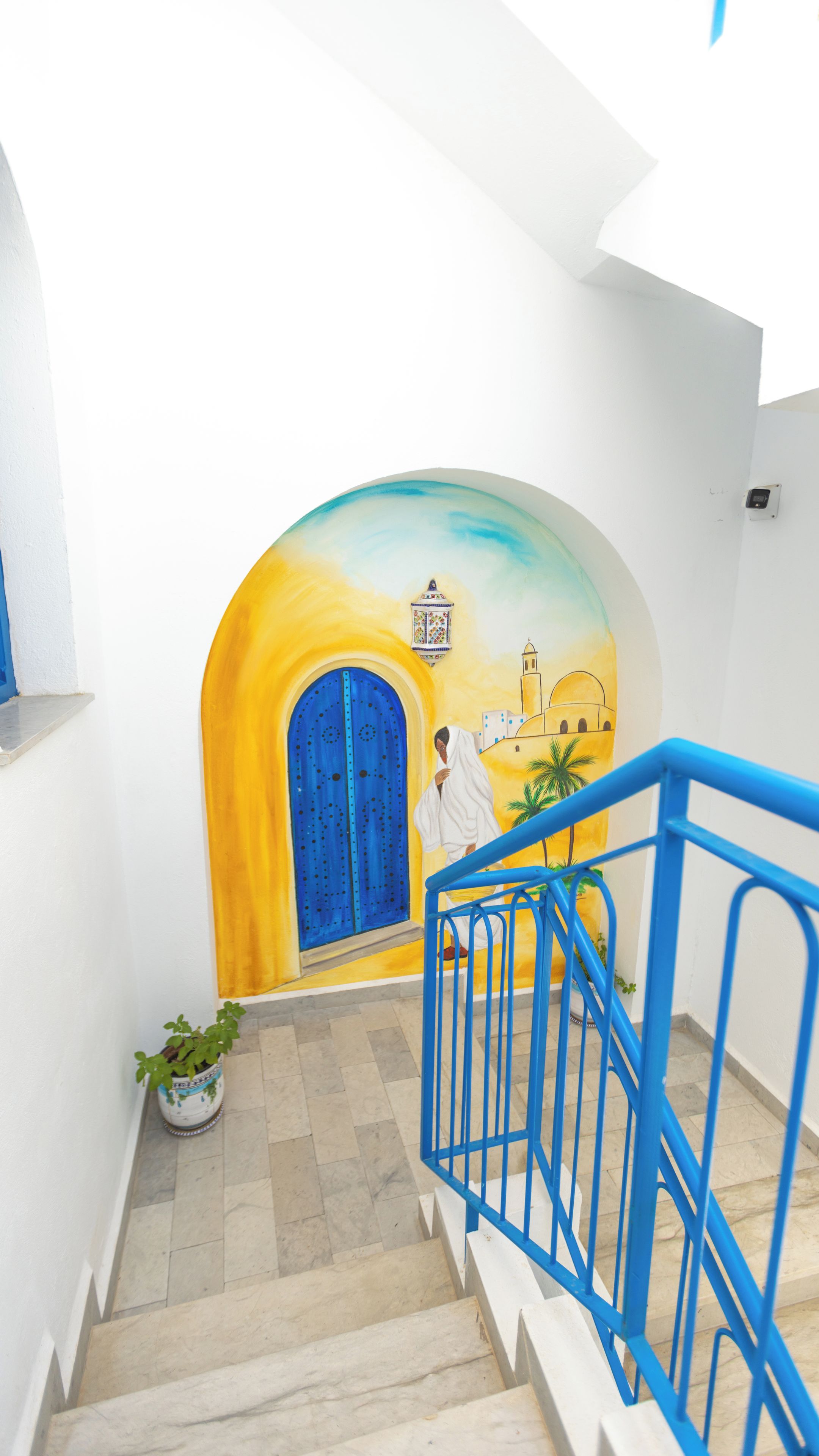 A staircase with a blue railing, a potted plant, and a colorful mural on the wall.