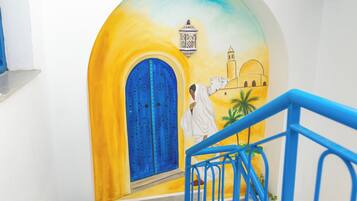 A staircase with a blue railing, a potted plant, and a colorful mural on the wall.