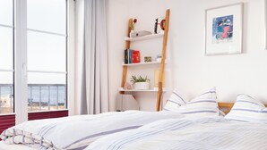 Un dormitorio con un ventanal grande, una estantería de madera con libros y objetos decorativos, y un cuadro enmarcado en la pared.