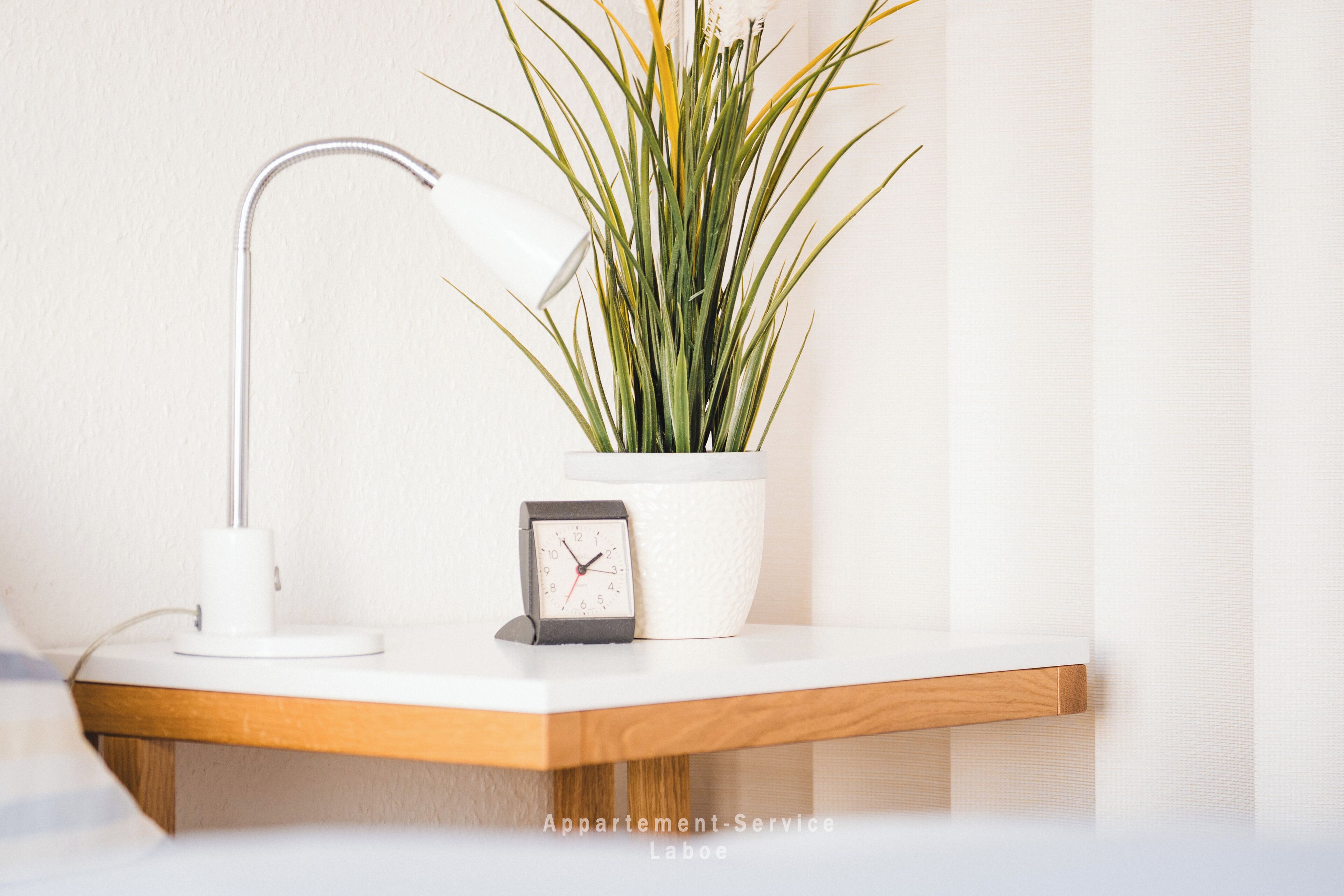 A white desk with a white desk lamp, a potted plant, and a clock.