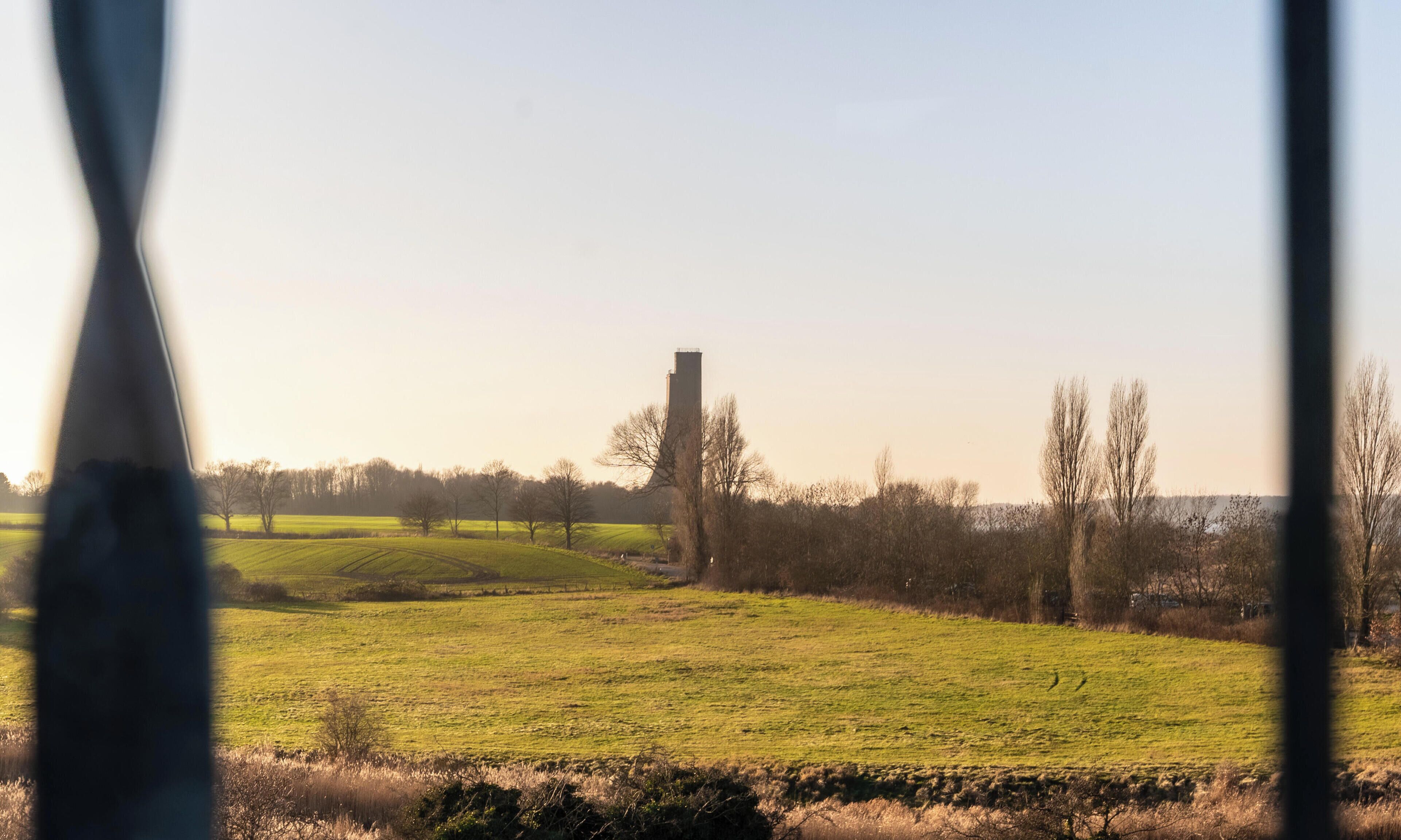 A rural landscape with a prominent tower structure in the center, surrounded by open fields and sparse trees.