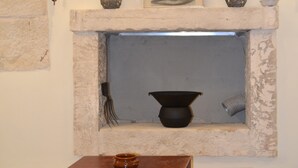 Ein Kamin aus Stein mit einem Rahmenbild darüber, eine kleine Schale auf dem Sims und ein Holztisch davor.