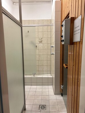 A small, narrow bathroom with a shower, tiled walls, and a wooden panel on one side. - Vacation apartment in Sahlenburg with sea view (Cuxhaven)