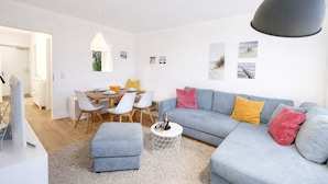 Una sala moderna con un sofá gris, una mesa de comedor con sillas y un mueble blanco para el televisor.