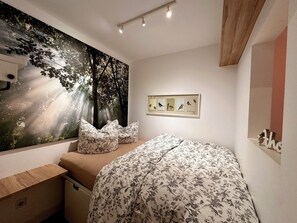 A bedroom with a bed, a desk, a chair, a wall mural, and a framed picture of birds. - Vacation apartment in Sahlenburg with sea view (Cuxhaven)